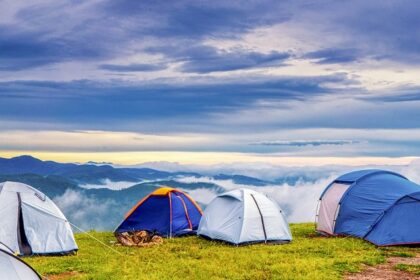 Several tents of blue and orange colour are placed next to each other on a hill