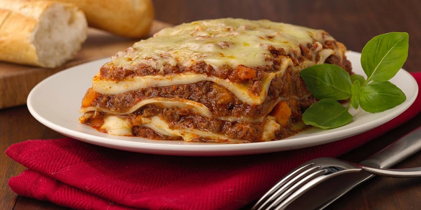 Lasagna, a pasta dish made with layers of flat sheets served in a tray topped with cheese.