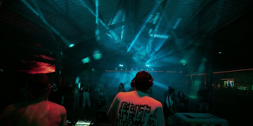 Image of a Dj perform at a club with vibrant lights and people dancing with their hands up