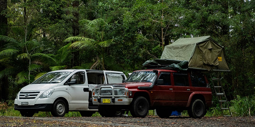 A white van and a red car are parked on the side of the road with a tent on the red car