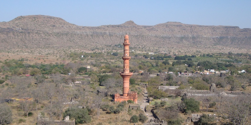 A towering red minaret surrounded by ruins and greenery, best place near Pitalkhora Caves.