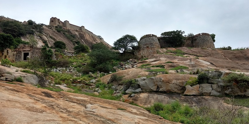 Channarayana Durga fortifications sit atop a rocky hill with sparse vegetation under sky.