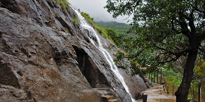 Bhaja Caves waterfall cascading down lush green hills, surrounded by rocky terrain