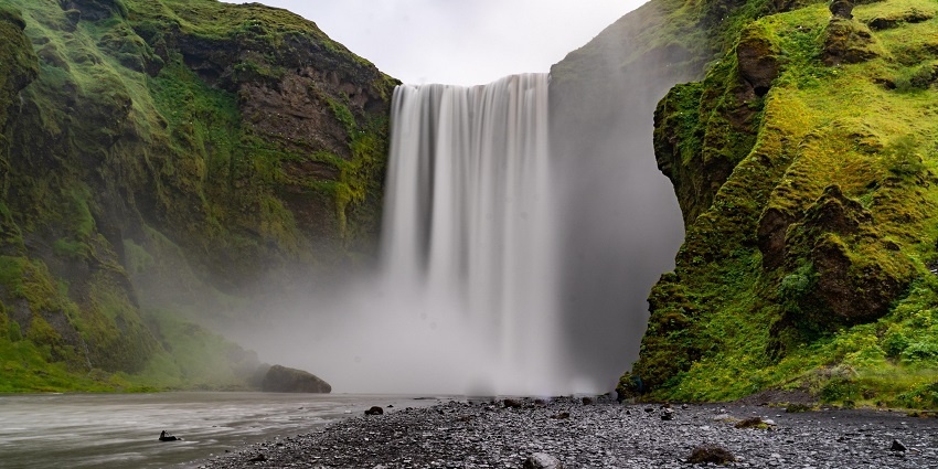 Water splashing against rocks at the base of a magnificent waterfall under clear blue skies.