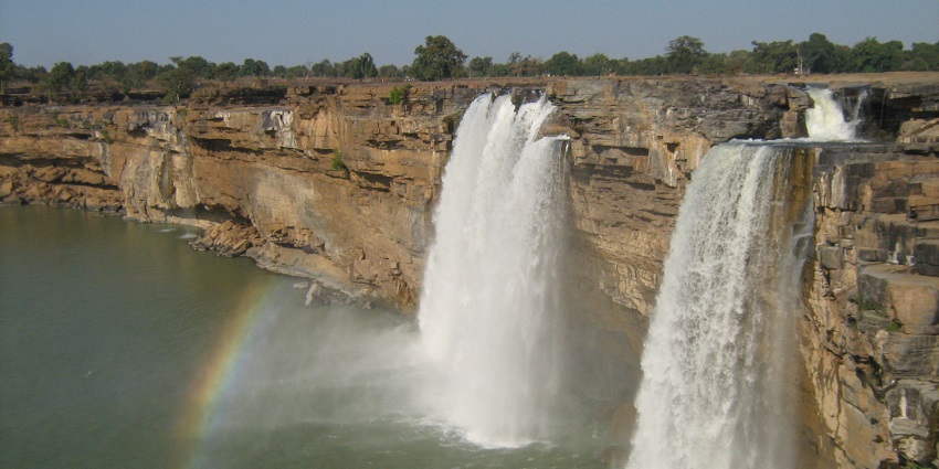 A wide-angle shot of Chitrakoot Falls surrounded by greenery, with clear skies overhead.