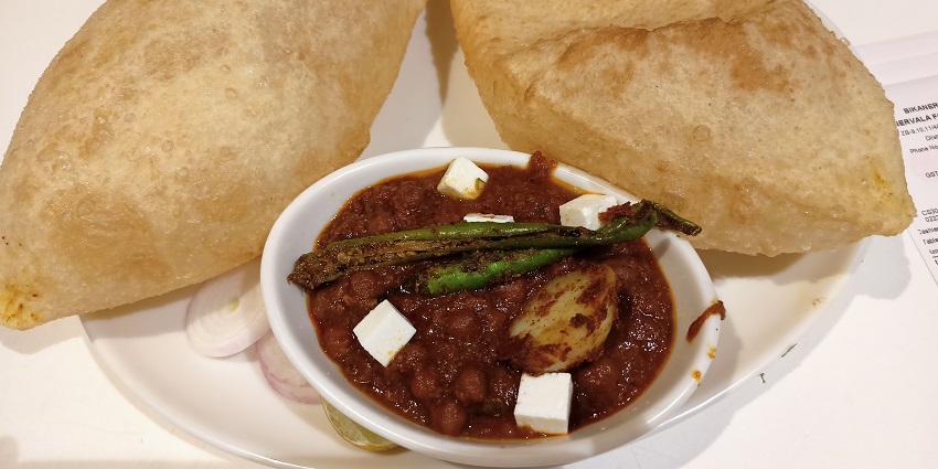 A mouth-watering view of a plate served with chhole bhature and sliced onions on the side.