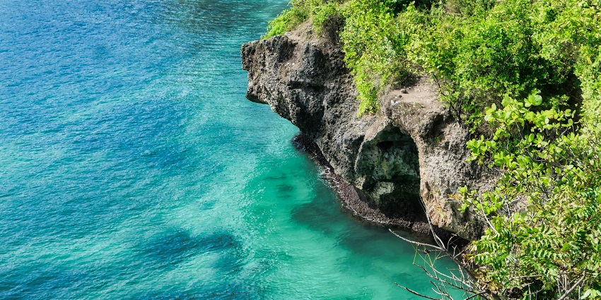 An image of an adventurer mid-jump off a cliff at Balangan Beach into the ocean below.