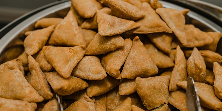 Small golden crispy samosas on a big silver plate with an old man taking them for serving