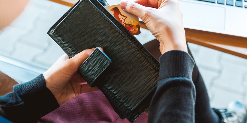 Person taking a card from their black leather wallet with a laptop on a table in view.