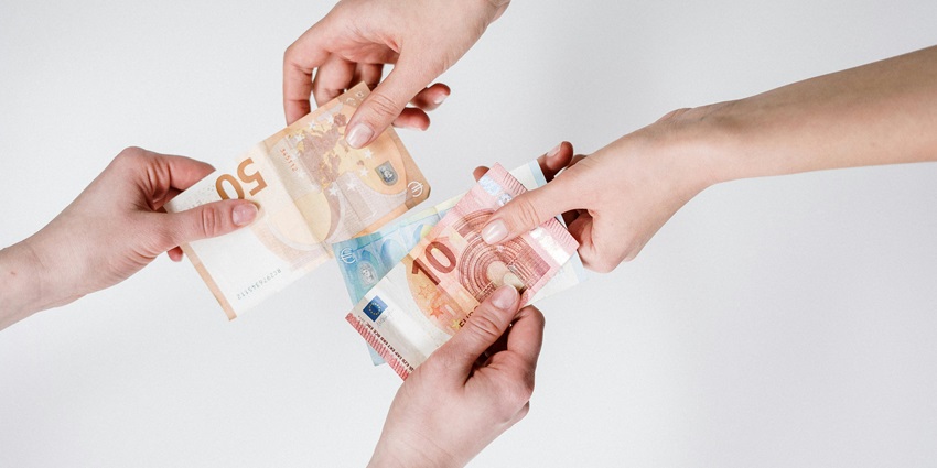 Two people exchanging different valued money bills.