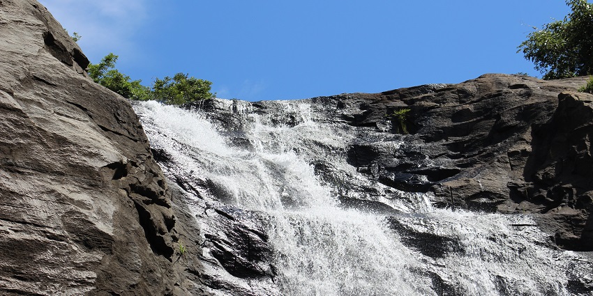 View of Courtallam Five Falls cascading through rocks, surrounded by lush greenery.