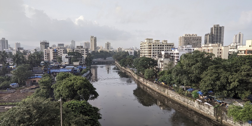 View of Dahisar River from the metro, flowing through an urban area with greenery along its banks