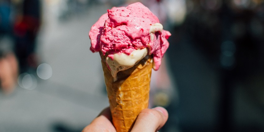 A person holding a cone of double scope of white and pink ice cream on a bright day