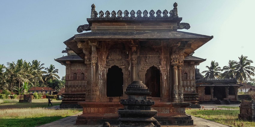 A view of a Hindu temple with detailed stone carvings, surrounded by greenery.