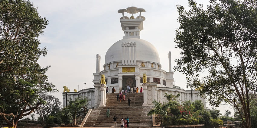 Front view of Dhauli Shanti Stupa with guardian lions and golden statues and people