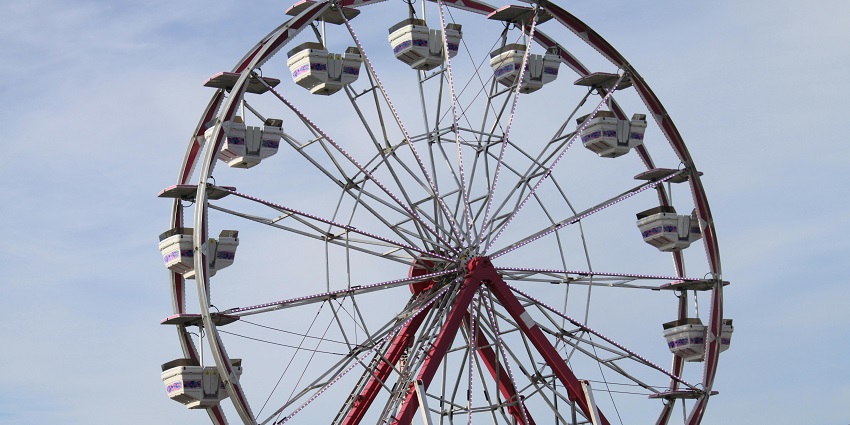 A glimpse of a ferris wheel illuminated at dusk, surrounded by colourful lights.