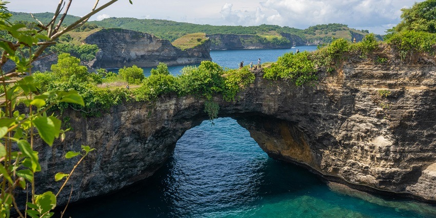 Aerial view of an archway forming with large rocks all around it, exploring these caves is a must thing to do in Uluwatu