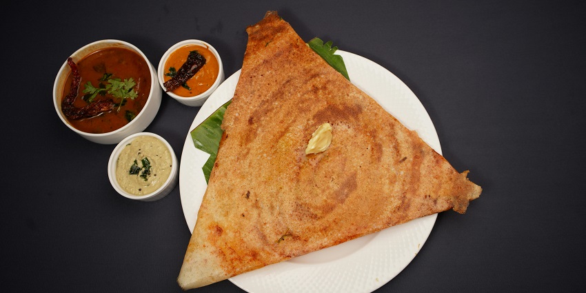 An image of a crispy rice crepe served with chutney and sambar, traditional dish.