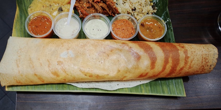 Golden, crispy dosa served with different chutneys and sambar on a traditional banana leaf