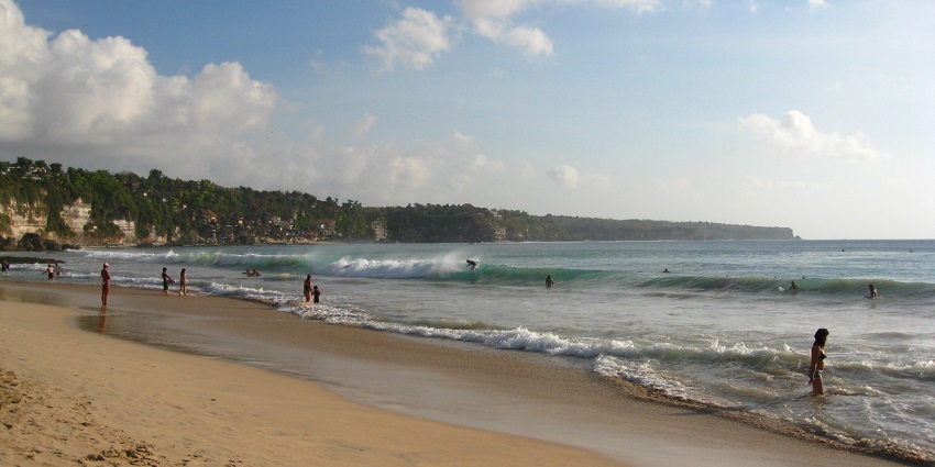 Panoramic view of Dreamland Beach, the vast expanses of sand reveal surfers happily playing in the waves.