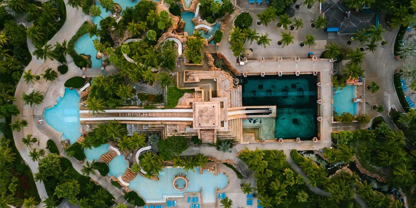 Aerial view of a swimming pool surrounded by lush trees at a park under a clear sky.