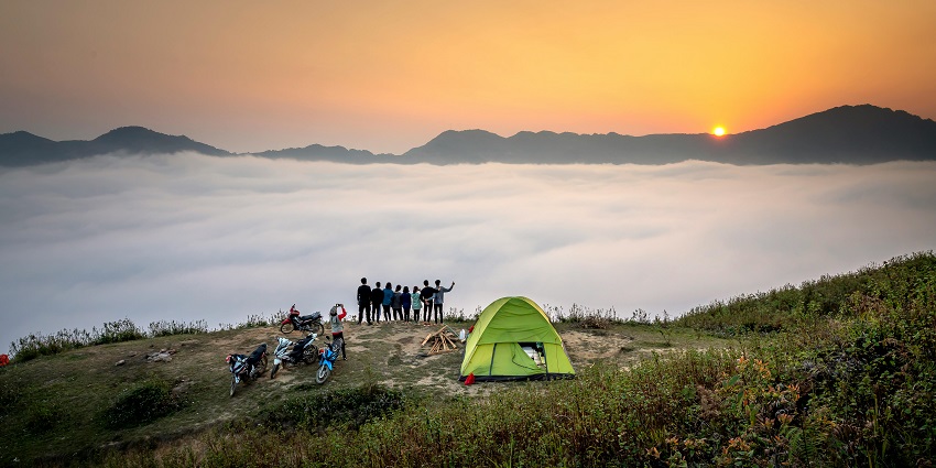 View of a group pf friends standing by a majestic cliff while camping