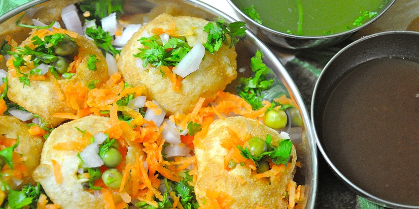Mouthwatering pani puri is served in a steel utensil garnished with coriander leaves.