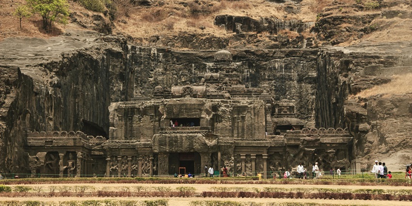 A picture of an ancient temple carved out of a mountain with greenery in its surroundings