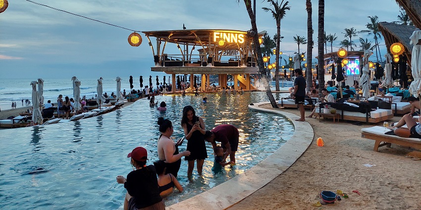 A picture of a beach club in Bali with people relaxing by the swimming pool.