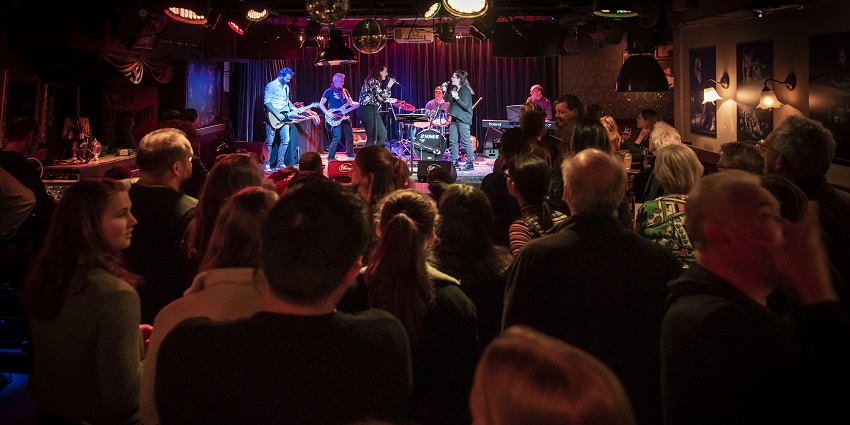 Live music playing in the venue with a large crowd sitting in the front enjoying