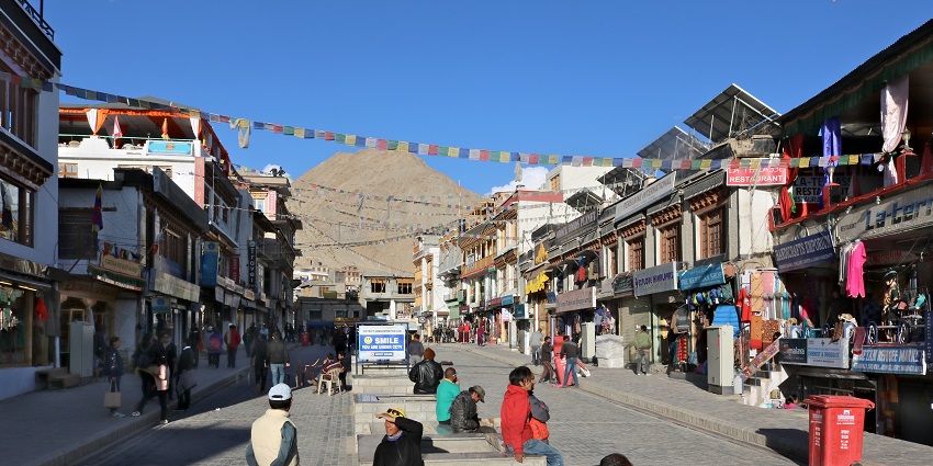 A picture of the main market street of Leh with bustling shops and a tall mountain visible in the background