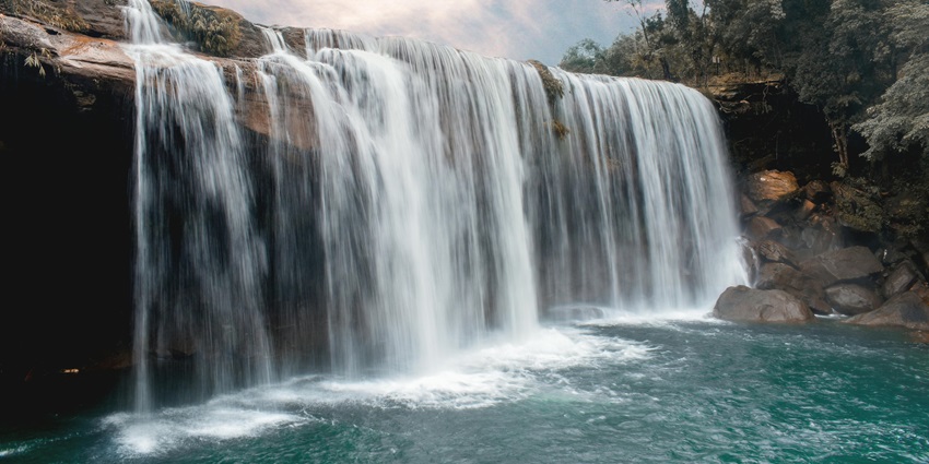 Image of waterfall cascading through rocks to the pond surrounded by dense forest