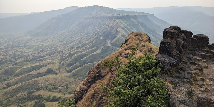 The image shows the Sajjangad Fort around, featuring a stone arch and lush greenery