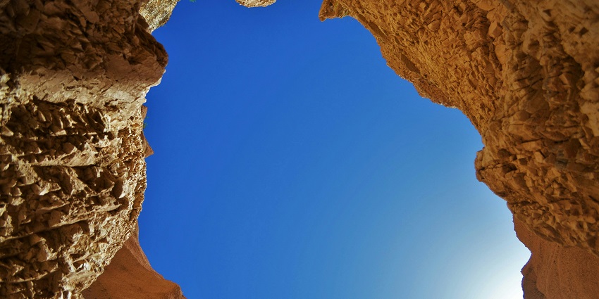A clear and deep blue sky can be seen above a cave with a brown-coloured rock formation.