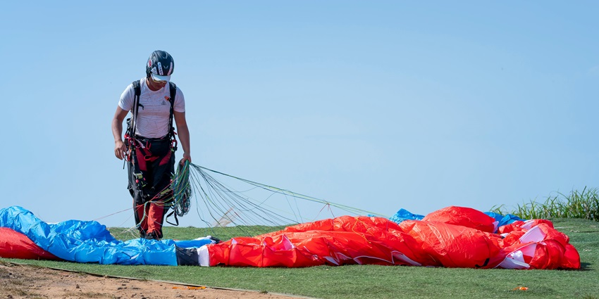 A man gripping the ties of a colourful parachute on green land with a clear blue sky.