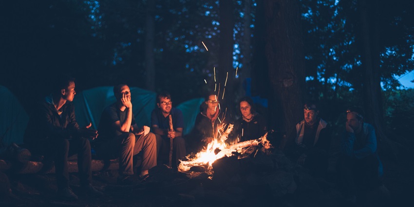 7 people sitting around a bonfire with camps at the back, similar to camping in Palghar.