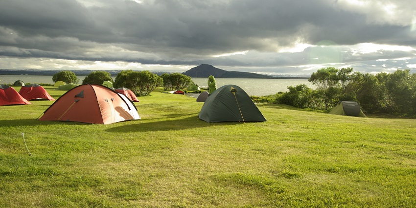 A person in a green jacket is standing among several tents while the weather is cloudy