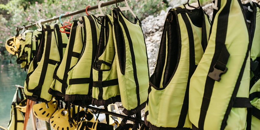 Wet bright-coloured vests hanging for drying on a wooden rack with other equipment.