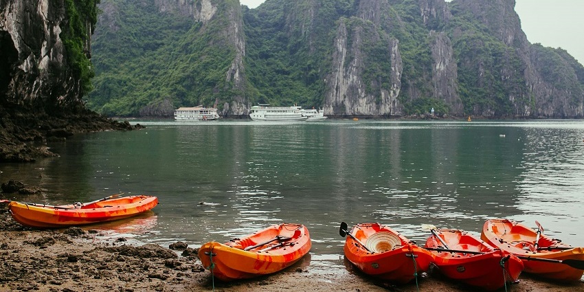 Orange kayaks lined up on the shore of a lake with green rocky mountains at a distance