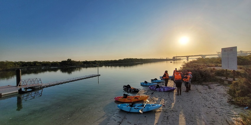 Kayakers waiting at the shore of waters with a soft orange sky reflecting on the lake.