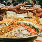 A man buying food from a street food vendor with his cart filled with a variety of Indian chaat