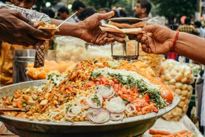 A man buying food from a street food vendor with his cart filled with a variety of Indian chaat