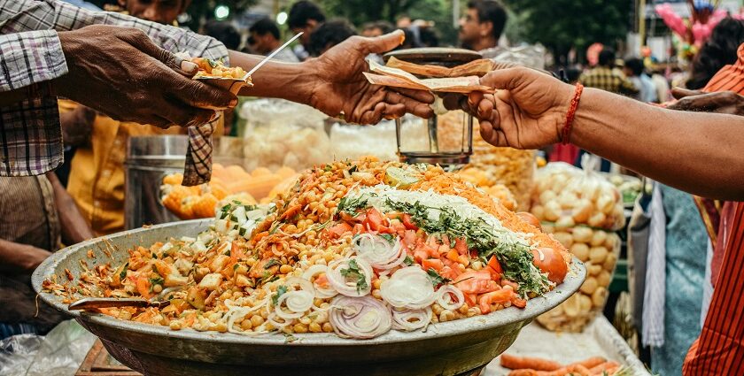 A man buying food from a street food vendor with his cart filled with a variety of Indian chaat