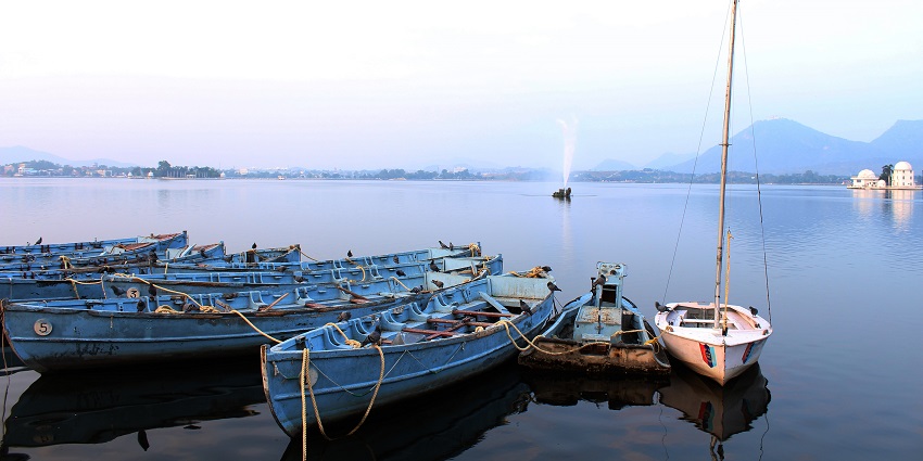 Boats at the shore of Fateh Sagar Lake surrounded by hills and an island in the middle