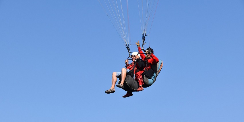 A view of two people enjoying tandem paragliding in a clear blue sky during the day.
