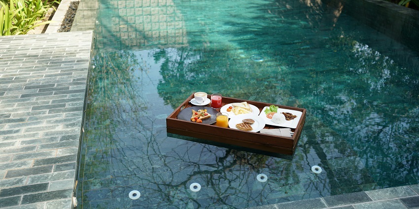An image of a luscious breakfast put on a wooden table floating over a private pool.