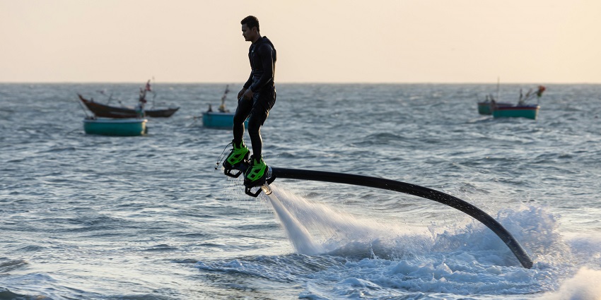 Image of a man enjoying the flying board in sea and small boats in the background