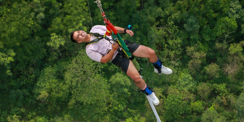A man zip-lining in a forest and is a popular destination near Mumbai for adventure.