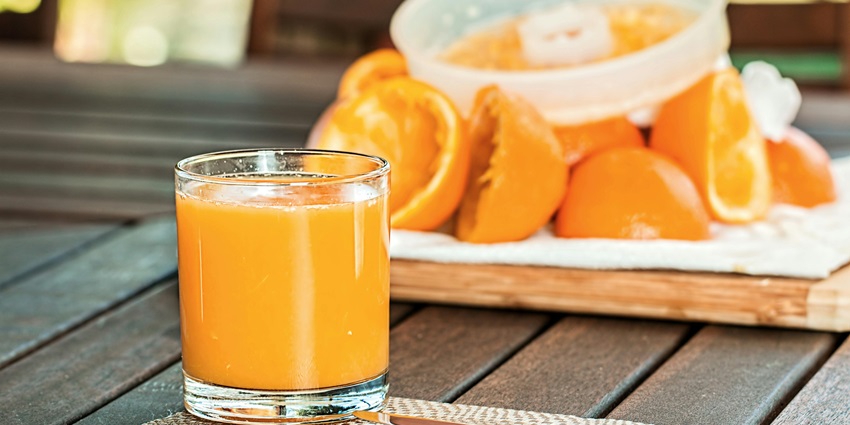 Pouring fresh, bright orange juice into a clear glass with citrus zest