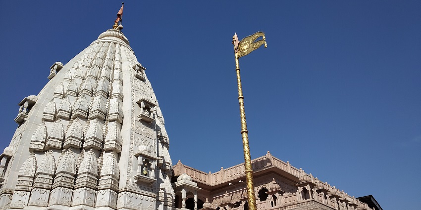 A picture of a historical temple with a Vijay Stambh standing tall in front of it